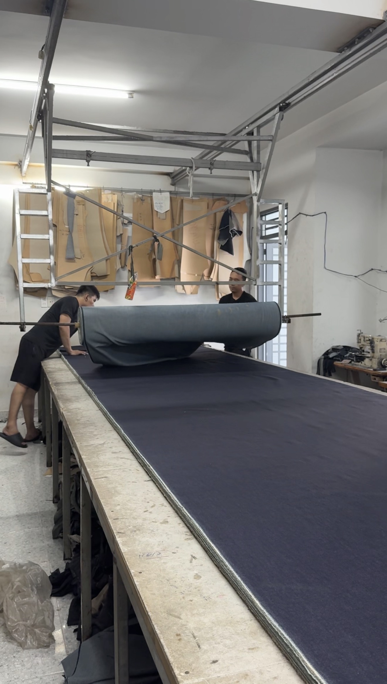 Denim rolled out across the cutting table with patterns hanging above